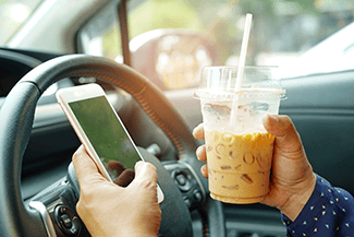 Person holding coffee and phone while driving