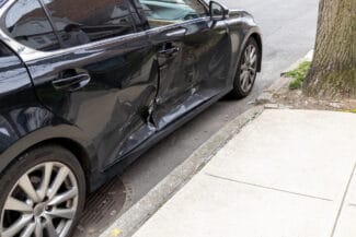 Black car with side damage parked on an urban street